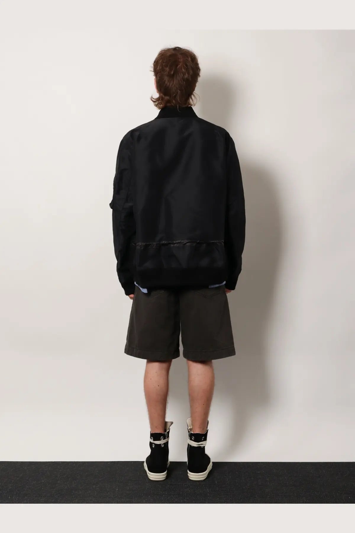 Sacai men’s black nylon bomber jacket with a matte finish and subtle reflective trim along the hem