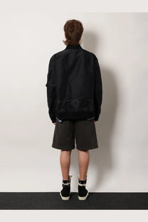 Sacai men’s black nylon bomber jacket with a matte finish and subtle reflective trim along the hem