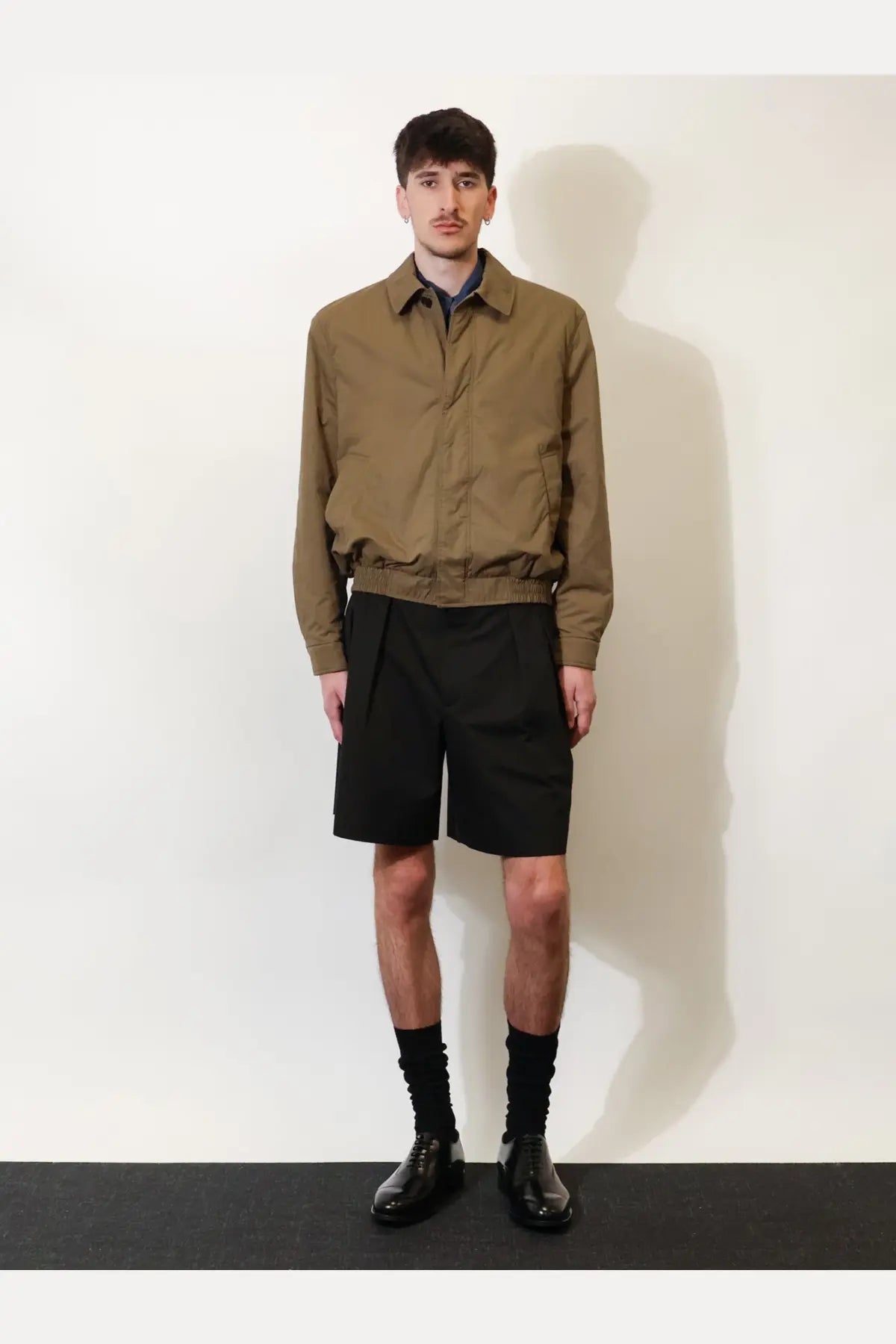 A man wearing a khaki beige saint laurent men’s cassandre cotton bomber jacket with collar and elasticated waistband
