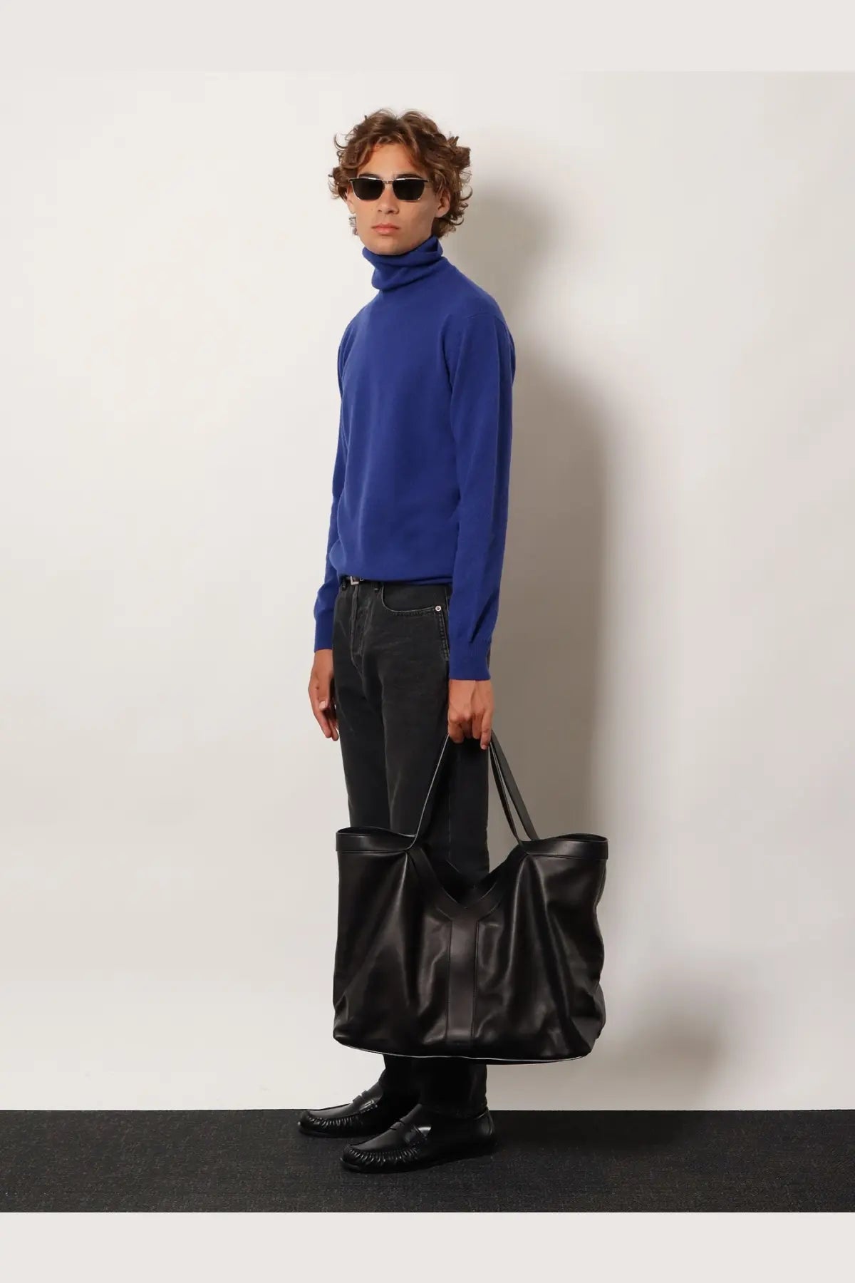 Black leather tote bag with structured handles and minimalist design paired with saint laurent men’s blue certified cashmere turtleneck