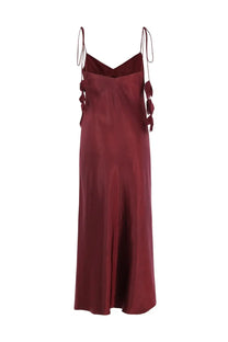 A flowing burgundy satin slip dress with delicate tied straps and decorative fabric tassels by Self-Portrait
