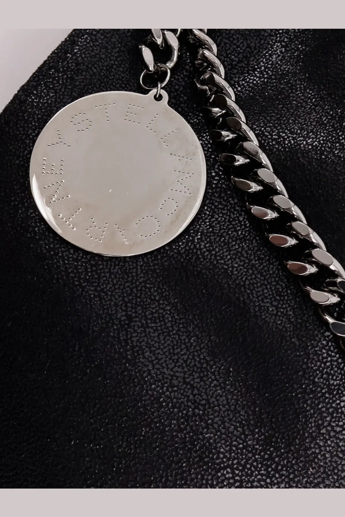Silver circular pendant embossed with stella mccartney lettering on a chunky black chain for falabella shoulder bag