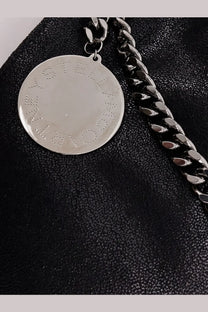 Silver circular pendant embossed with stella mccartney lettering on a chunky black chain for falabella shoulder bag