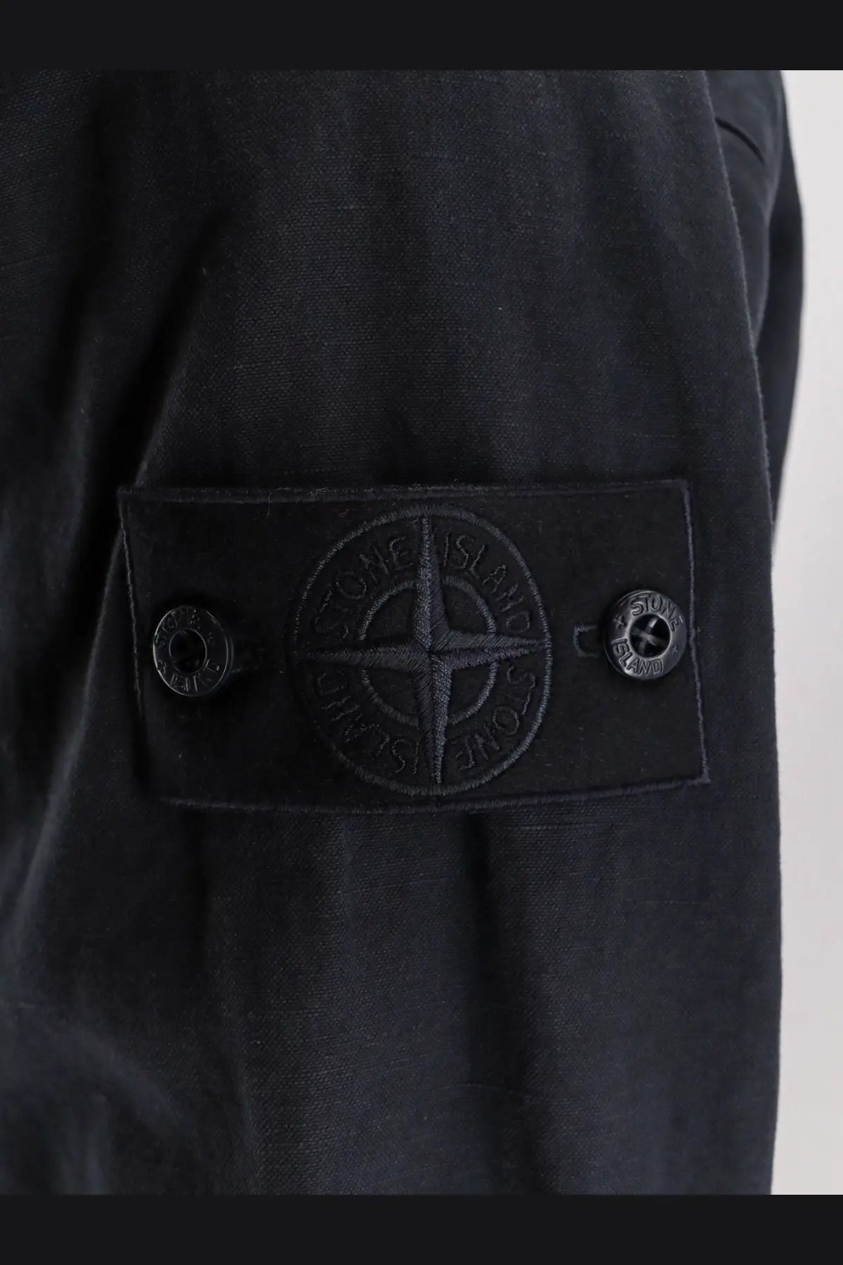 Black stone island patch with embroidered compass logo and two snap buttons on stone island men’s blue cotton linen shirt