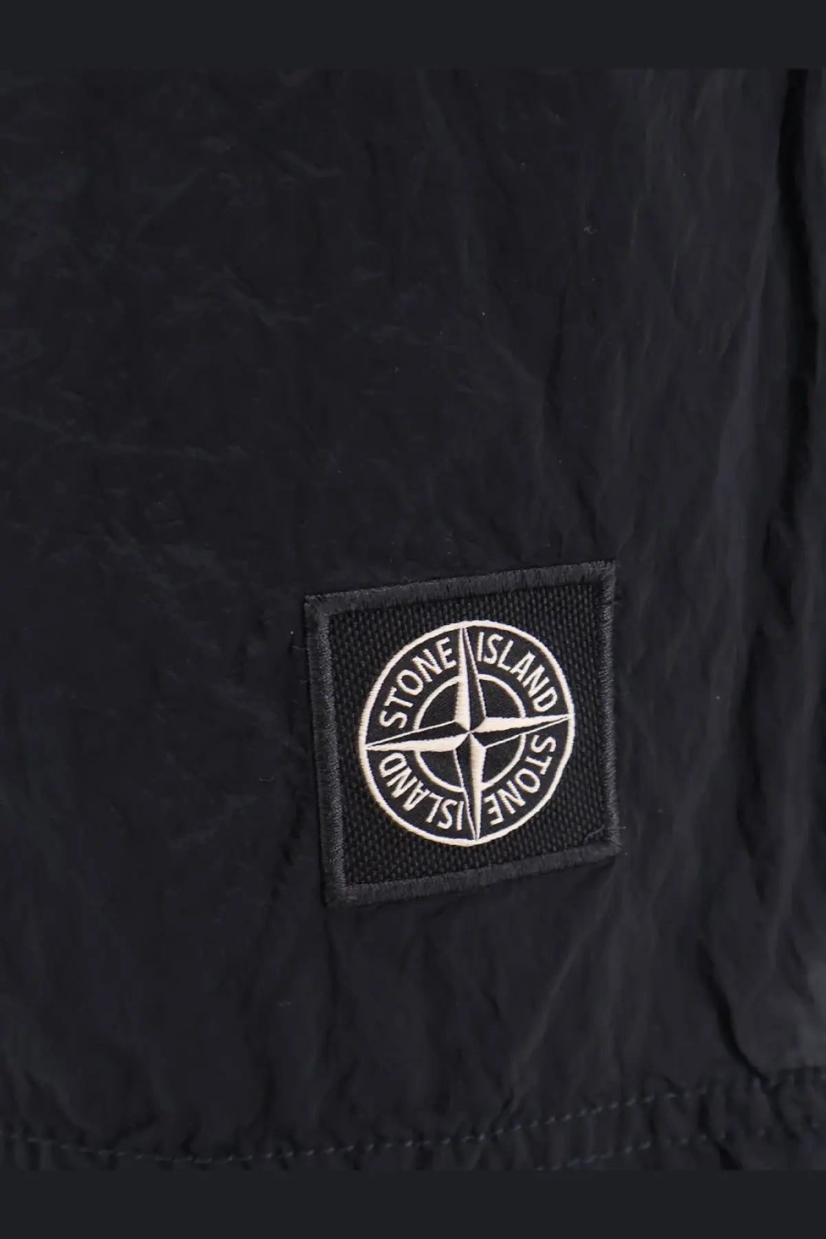 Black stone island patch with white compass rose logo on fabric of stone island mens econylon swim trunks blue