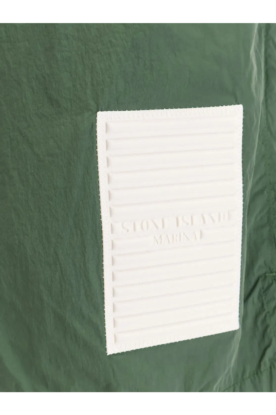 White rectangular embossed stone island marina label with ridges on dark green fabric of stone island men’s nylon swim trunks beige