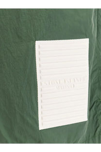 White rectangular embossed stone island marina label with ridges on dark green fabric of stone island men’s nylon swim trunks beige