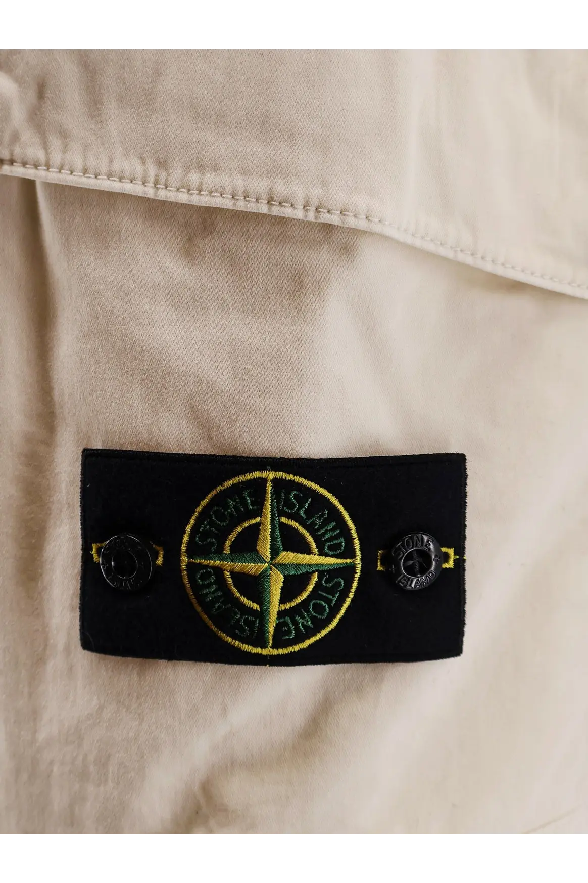 Black rectangular label with yellow and green Stone Island compass rose logo on men’s organic cotton white Bermuda shorts