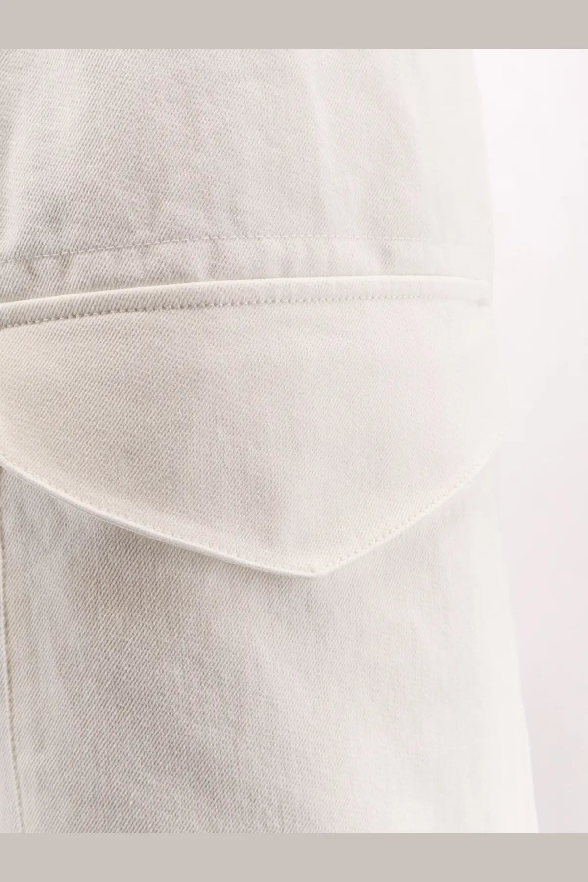 A close-up of a light-wash denim pocket on studio nicholson men’s cotton bermuda shorts salt with stitched edges