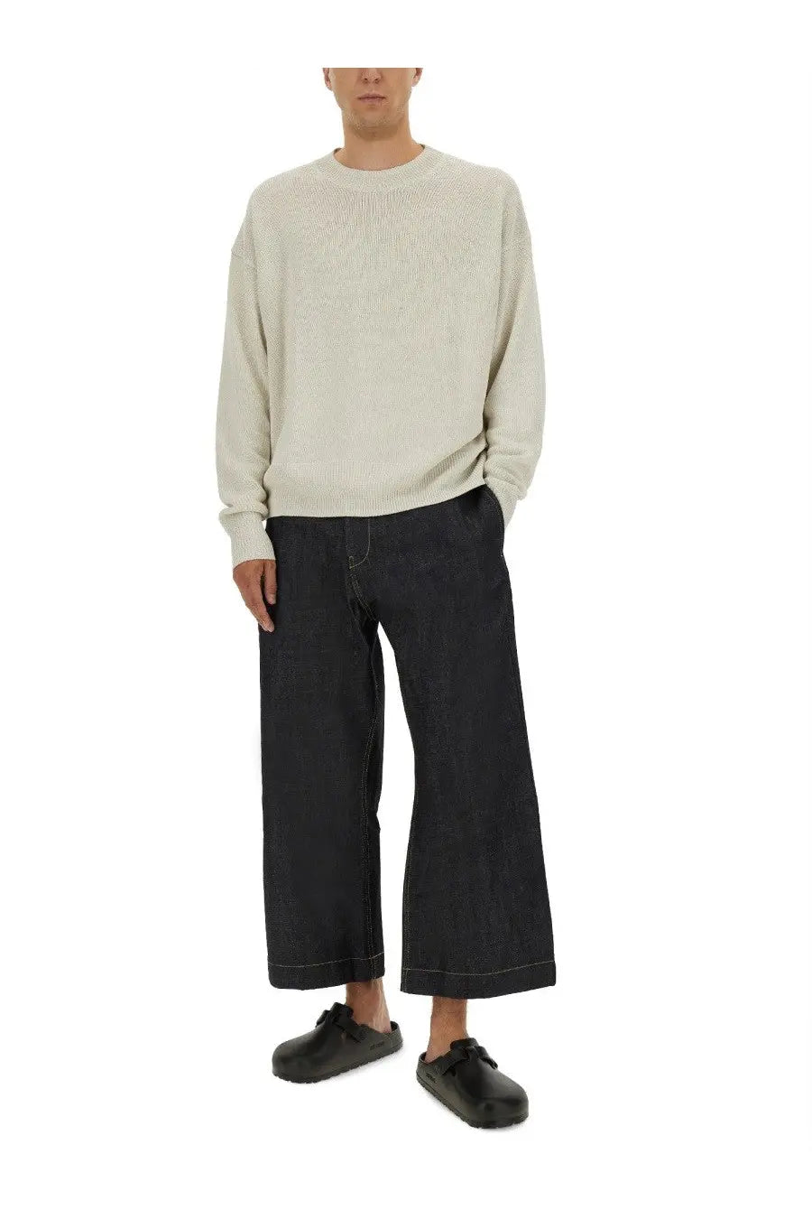 A man wearing a cream ribbed knit sweater with long sleeves and dark denim wide-leg pants in studio nicholson kami shirt white style