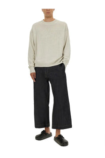 A man wearing a cream ribbed knit sweater with long sleeves and dark denim wide-leg pants in studio nicholson kami shirt white style
