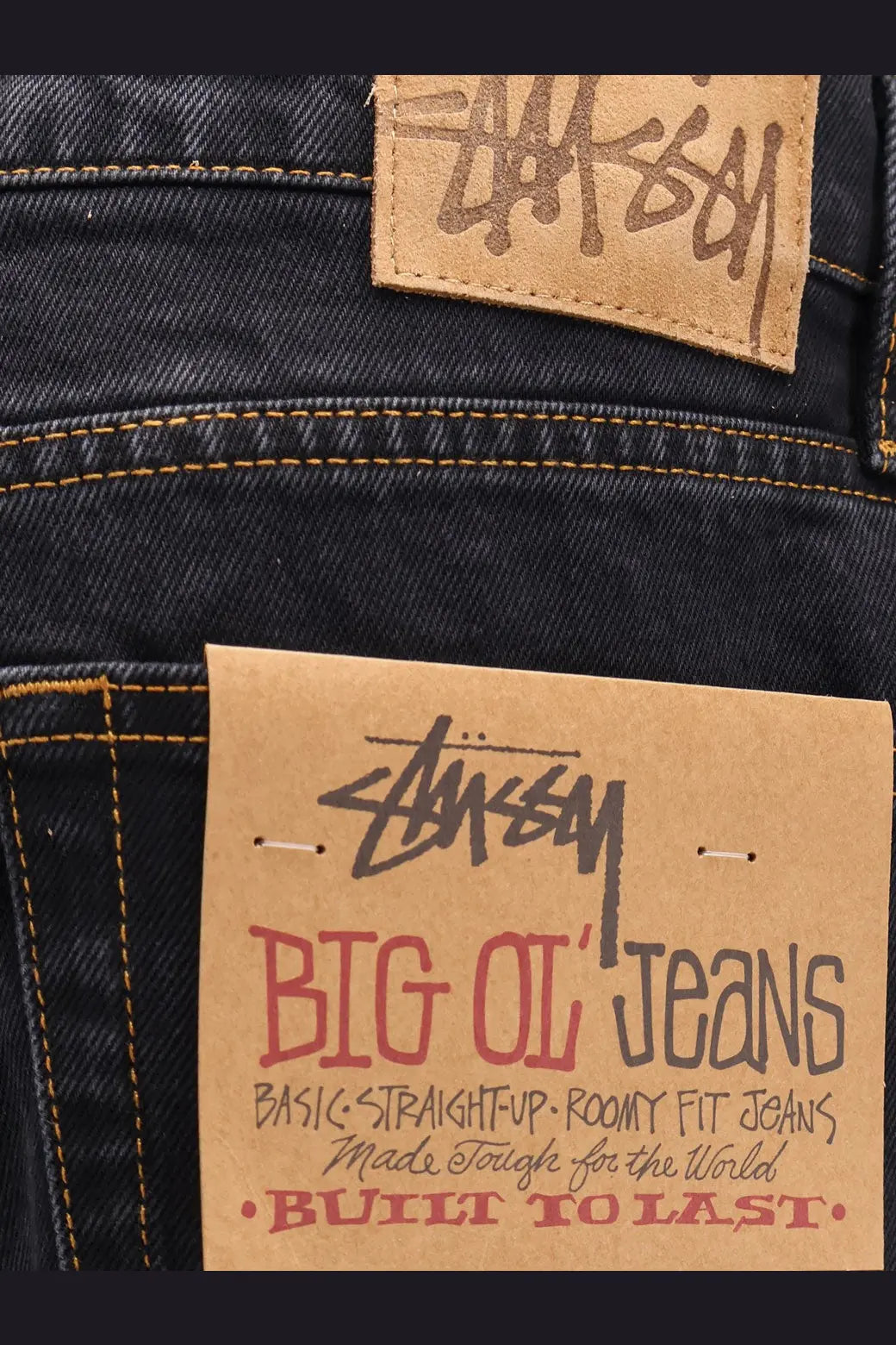 Dark-wash stussy men’s big ol jean black denim with brown leather brand patch and red black cardboard label on back