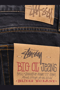 Dark-wash stussy men’s big ol jean black denim with brown leather brand patch and red black cardboard label on back