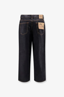 Dark-wash stussy men’s big ol jeans with wide-leg cut and brown leather logo patches on black denim