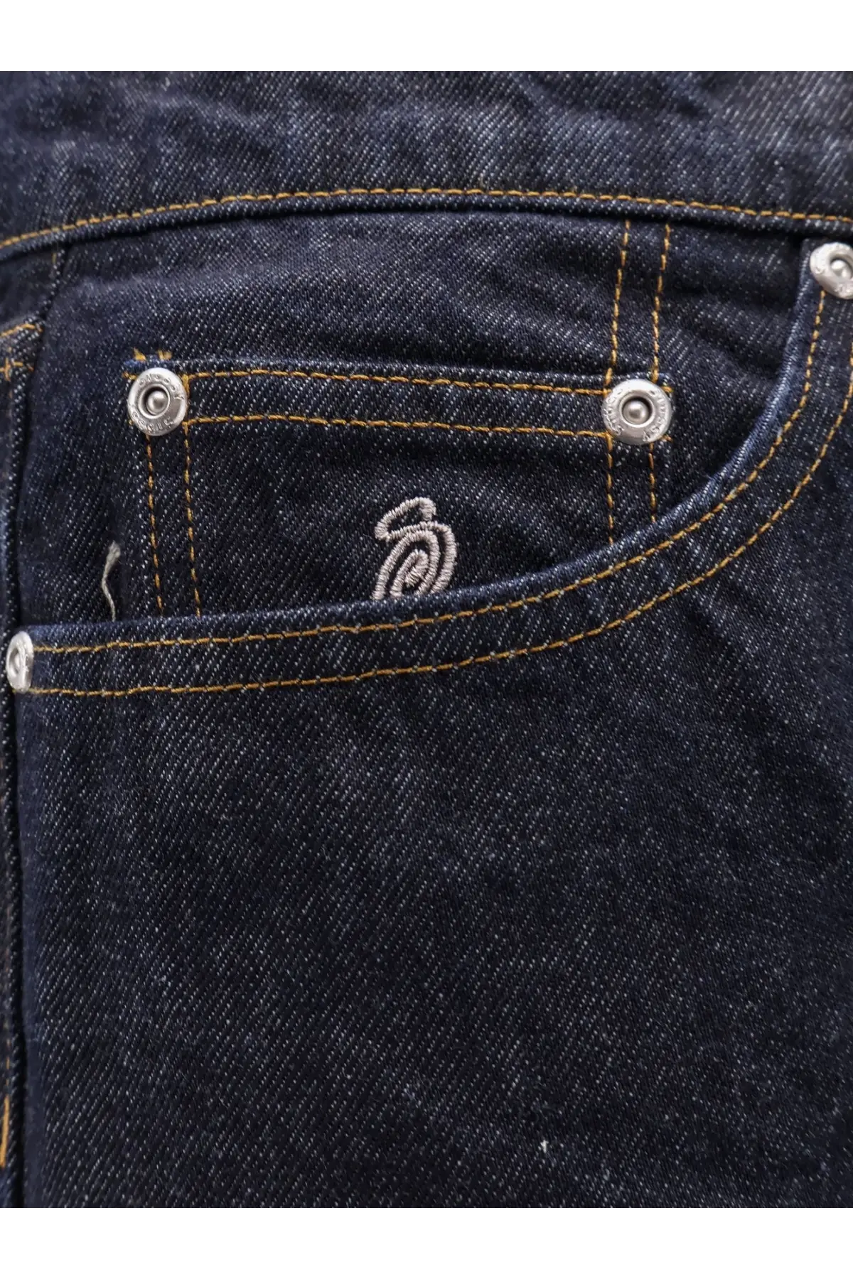Dark blue denim jeans pocket with silver metal rivets and subtle embroidered logo on stussy mens new classic jeans back side