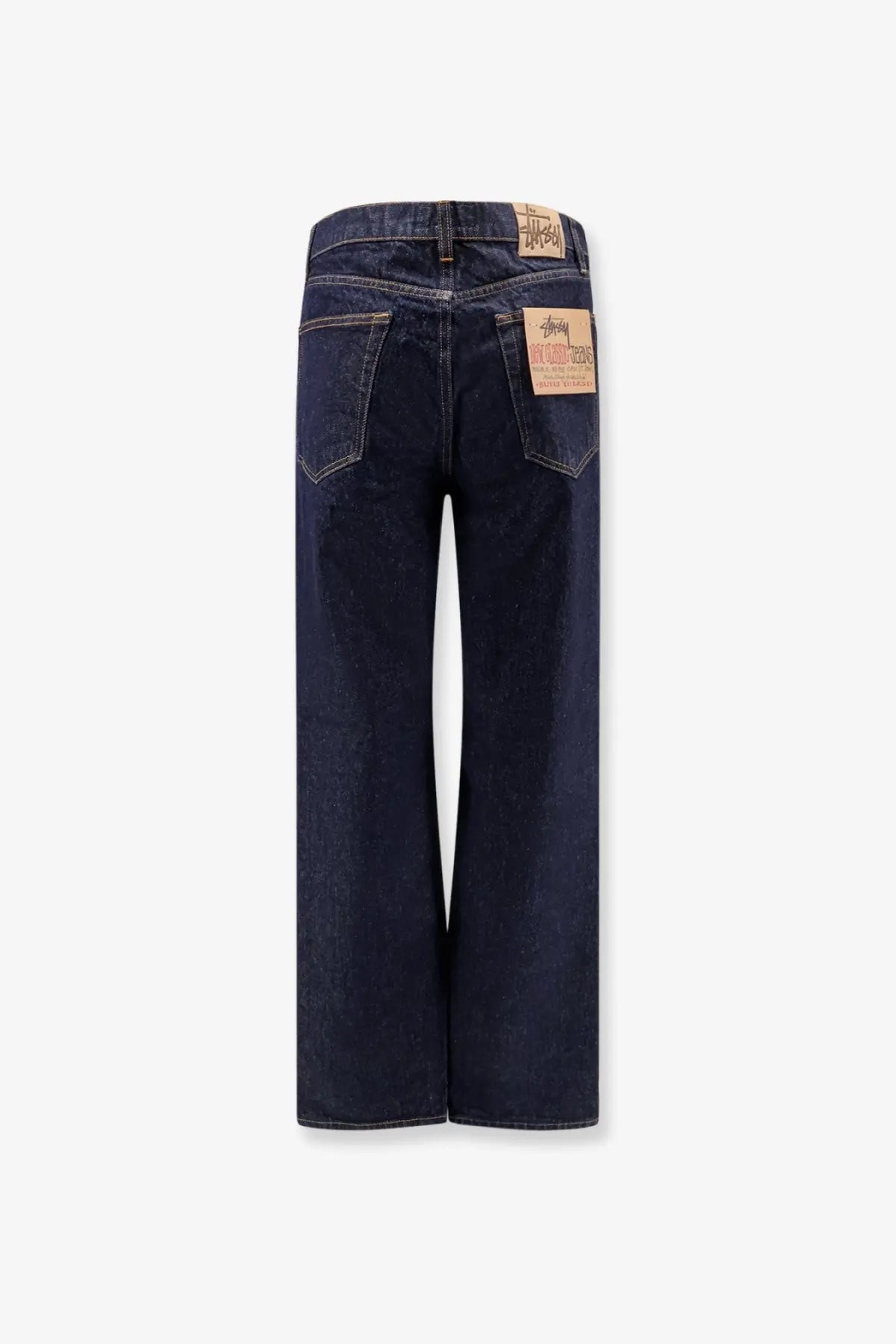 Back view of stussy men’s new classic regular fit jeans in dark indigo denim with brown leather patches on pockets