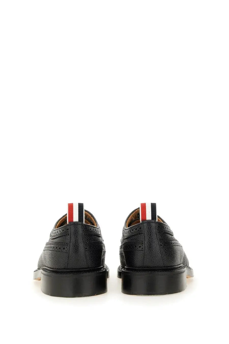 Back view of thom browne men’s brogue classic longwing black leather oxford shoes with red white and black striped pull tab