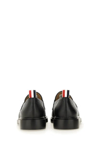 Black leather Thom Browne men’s moccasin penny loafer showing back with red white and blue striped tab heel