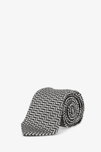 A neatly rolled tom ford men’s silk tie in grey with a black and white herringbone pattern