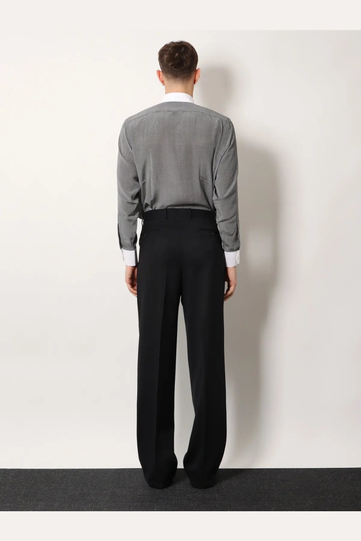 A man wearing Tom Ford men’s black wool trousers paired with a gray patterned long-sleeve shirt with white cuffs