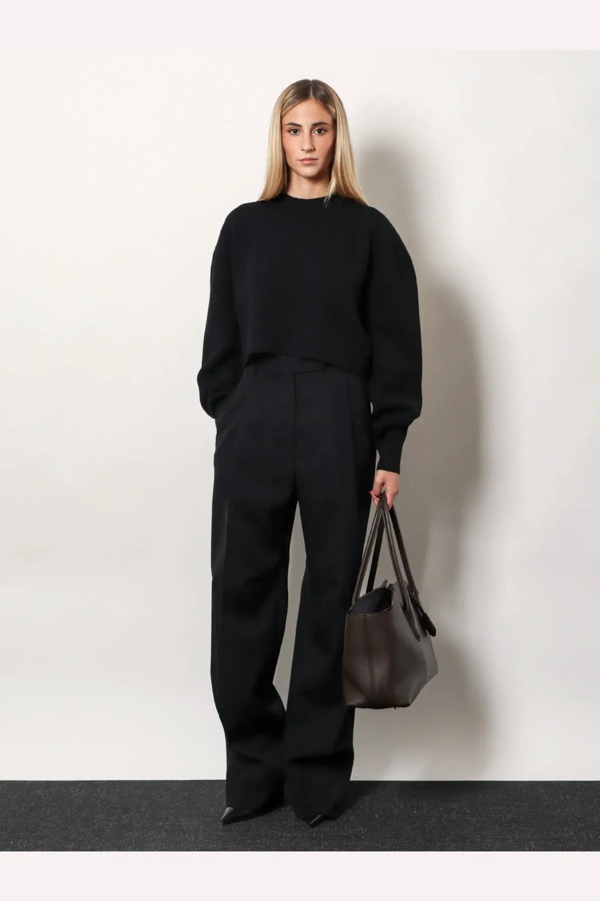 Black leather tote bag with structured shape and dual top handles shown with tom ford women’s pleated wool trousers black