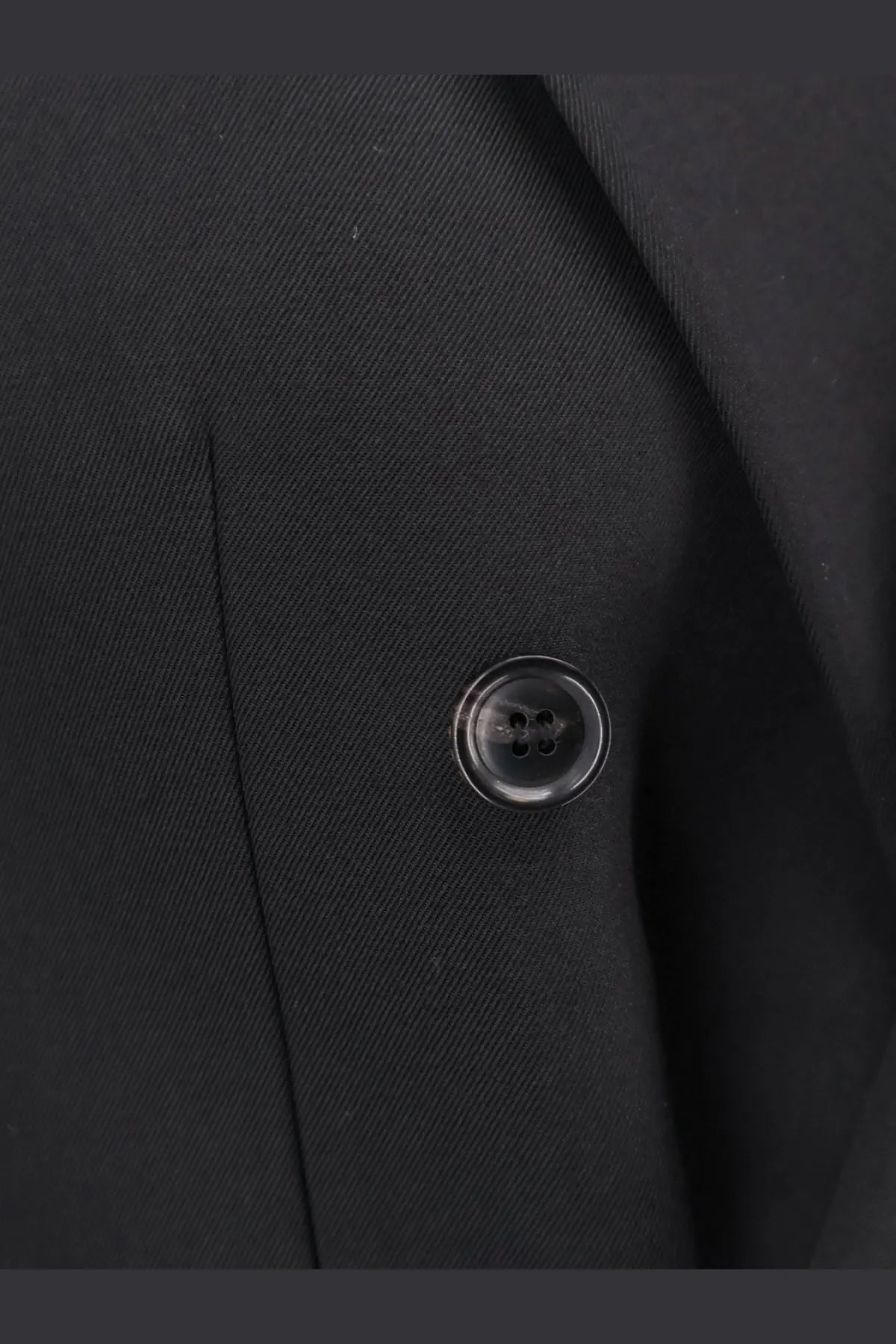 Black glossy four-hole button on tonywack men’s tailored wool blend blazer black against dark fabric background