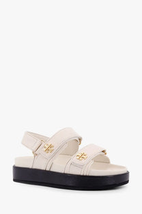 Tory Burch women’s Kira low leather sandals in cream with gold-tone logo buckles and black platform sole