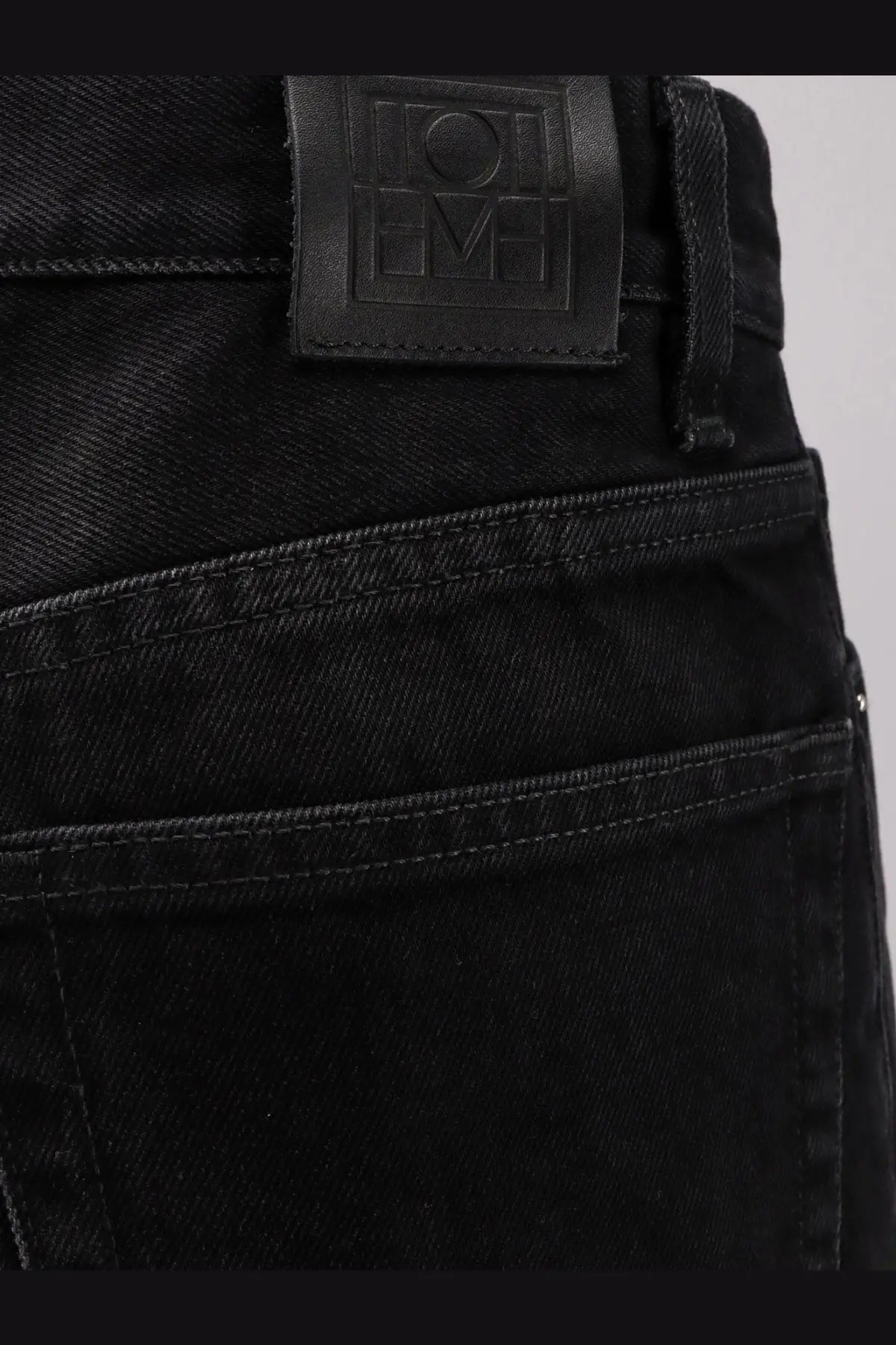 Toteme womens black denim jeans in dark wash with visible stitching and branded leather patch at the waistband back view
