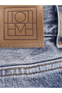 Brown leather patch with embossed loewe logo on the back of grey Toteme women’s cotton jeans on blue denim fabric