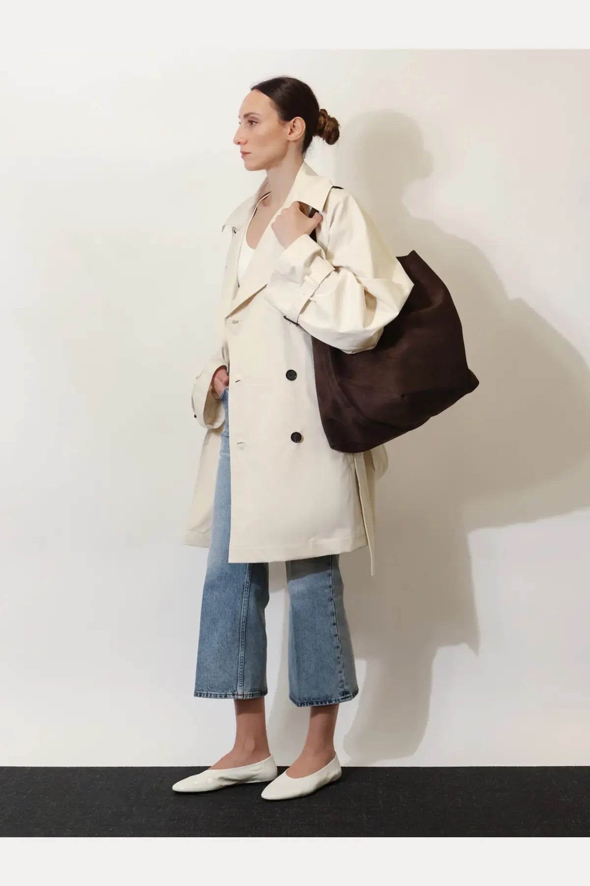 Cream-colored trench coat with black buttons and wide relaxed sleeves paired with toteme women’s grey cotton jeans