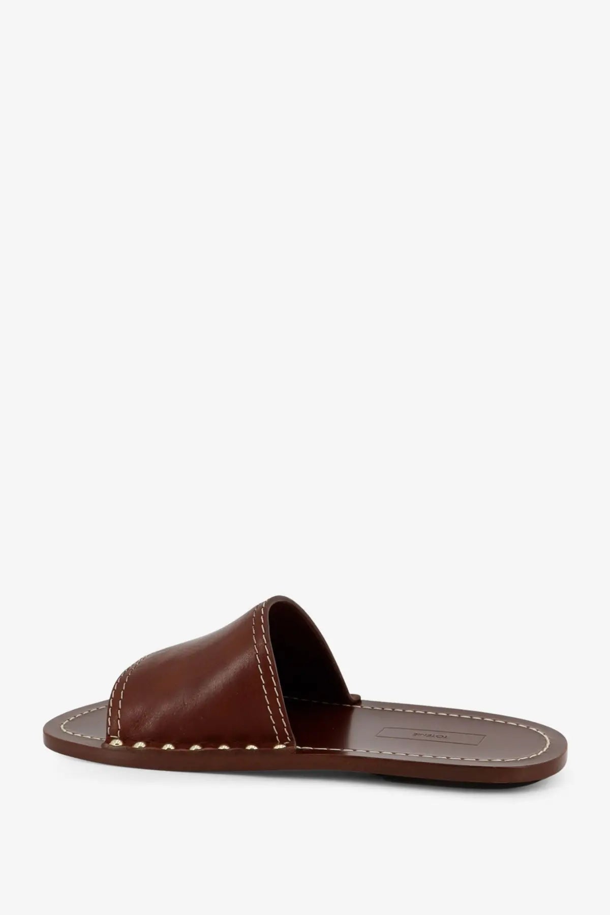 Toteme women’s low brown leather slide sandal with white stitching and metallic studs along the edge