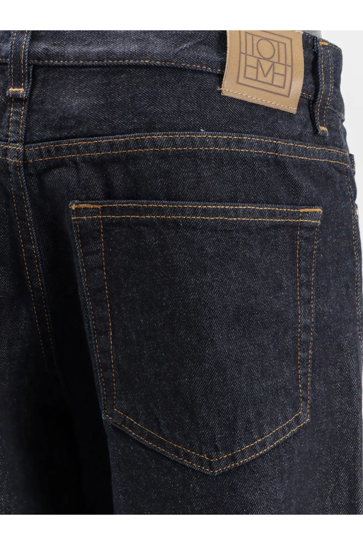 Toteme women’s low straight denim jeans in dark indigo with tan stitching and a brown leather brand patch on the back waistband