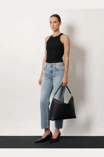 Black leather hobo bag with structured minimalist design and single top handle shown with Toteme women’s grey jeans