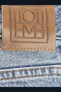 Tan leather brand patch with embossed loewe logo stitched on blue denim back of toteme womens low straight organic cotton jeans gray