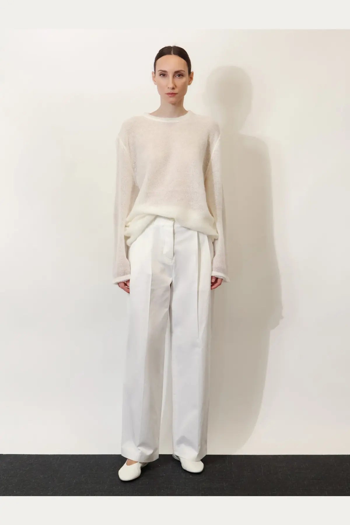 A minimalist white knit sweater with long sleeves and a relaxed fit paired with toteme women’s relaxed cotton trousers white