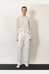 A minimalist white knit sweater with long sleeves and a relaxed fit paired with toteme women’s relaxed cotton trousers white