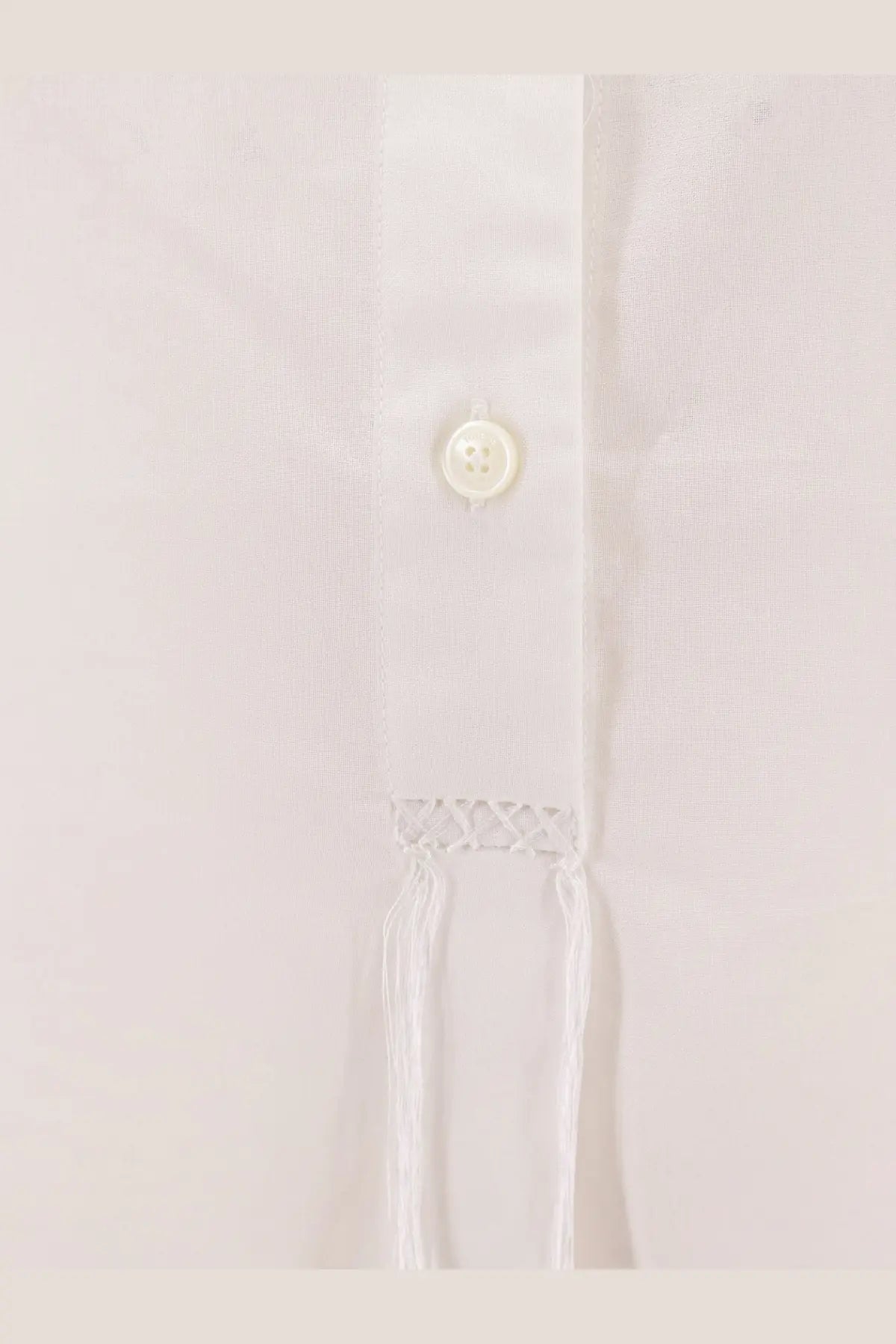 A delicate white button with subtle sheen on the textured fabric of a toteme women’s stand collar organic cotton shirt white