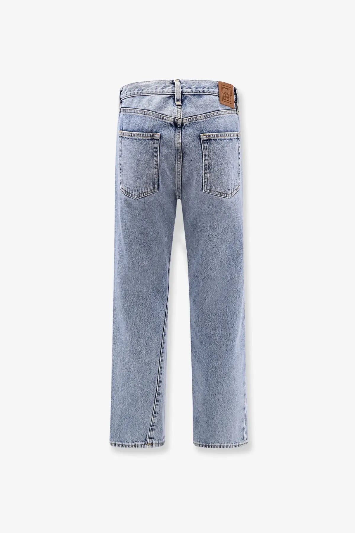 Back view of toteme women’s twisted seam light-wash organic cotton jeans with straight legs and brown leather patch
