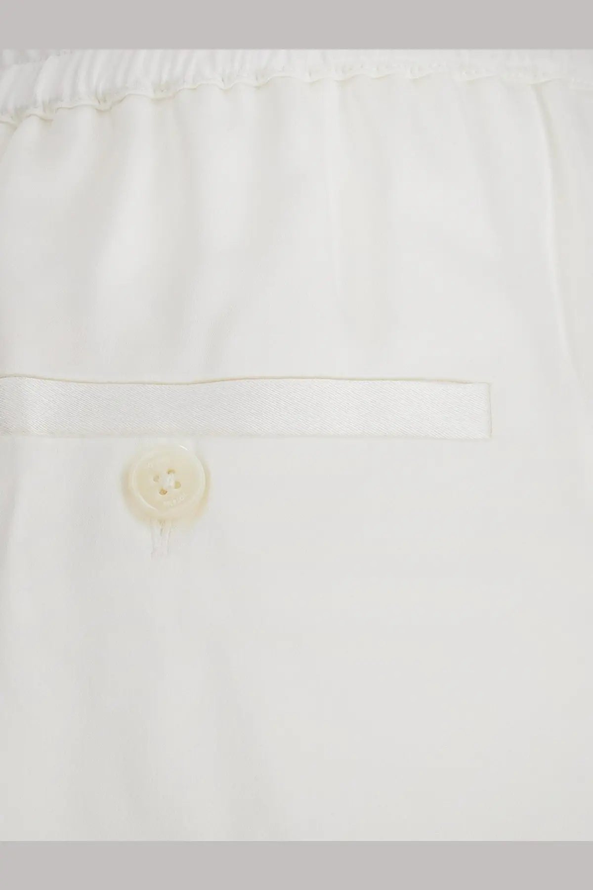 Toteme women’s white viscose trousers with subtle pleated waistband and single button closure visible from the back