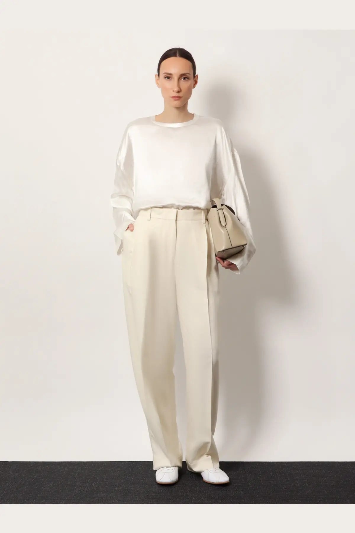 A minimalist beige leather handbag with a structured rectangular shape and top handle paired with toteme white viscose trousers