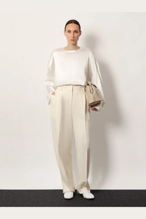 A minimalist beige leather handbag with a structured rectangular shape and top handle paired with toteme white viscose trousers