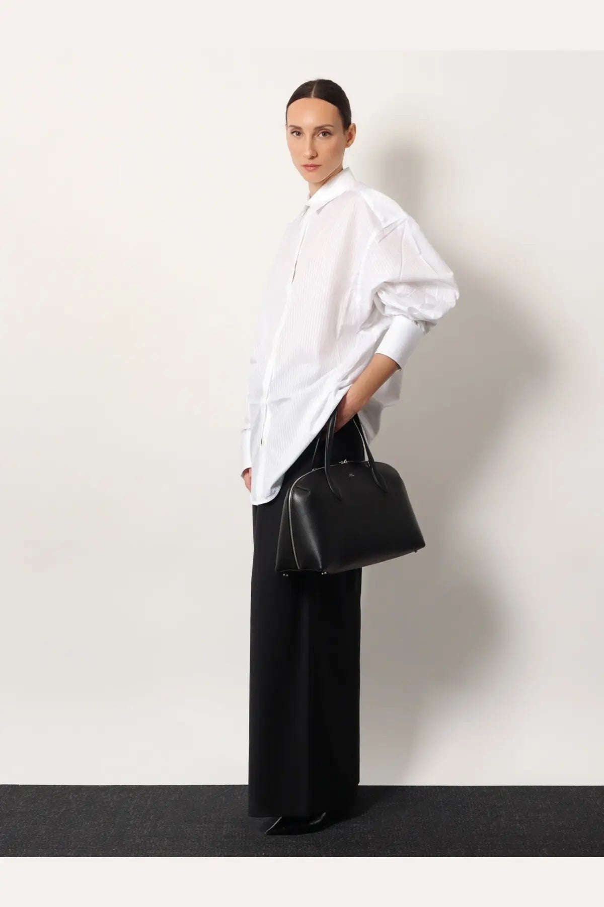 Black leather handbag with structured shape and top handles paired with toteme women’s wool trouser black
