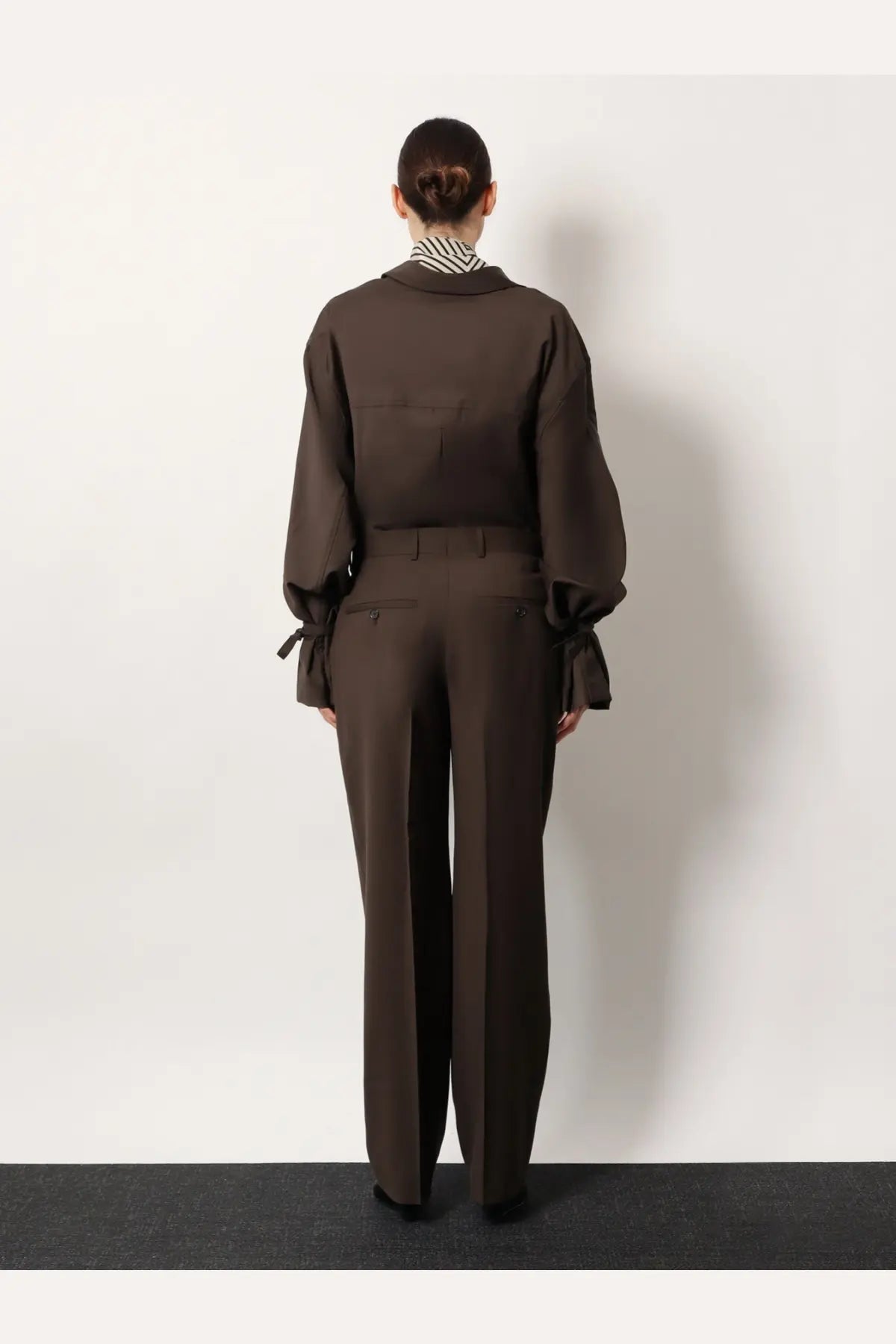 Brown linen jumpsuit with tied cuffs and collar paired with toteme women’s grey wool trousers