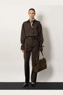 Brown suede shoulder bag with flap closure and adjustable strap paired with toteme women’s grey wool trousers