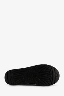 Black rubber sole of ugg men’s tasman noir leather slip with starburst tread pattern and ugg logo near the heel