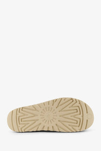 Beige rubber sole with starburst tread pattern and embossed ugg logo on ugg women’s goldenstar gleam sandals in suede brown