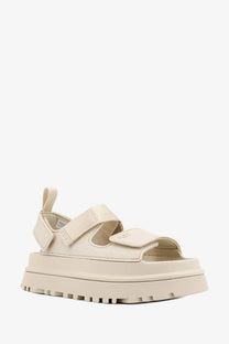 Cream-colored ugg women’s rubber platform sandal with wide velcro straps and chunky rubber sole in beige