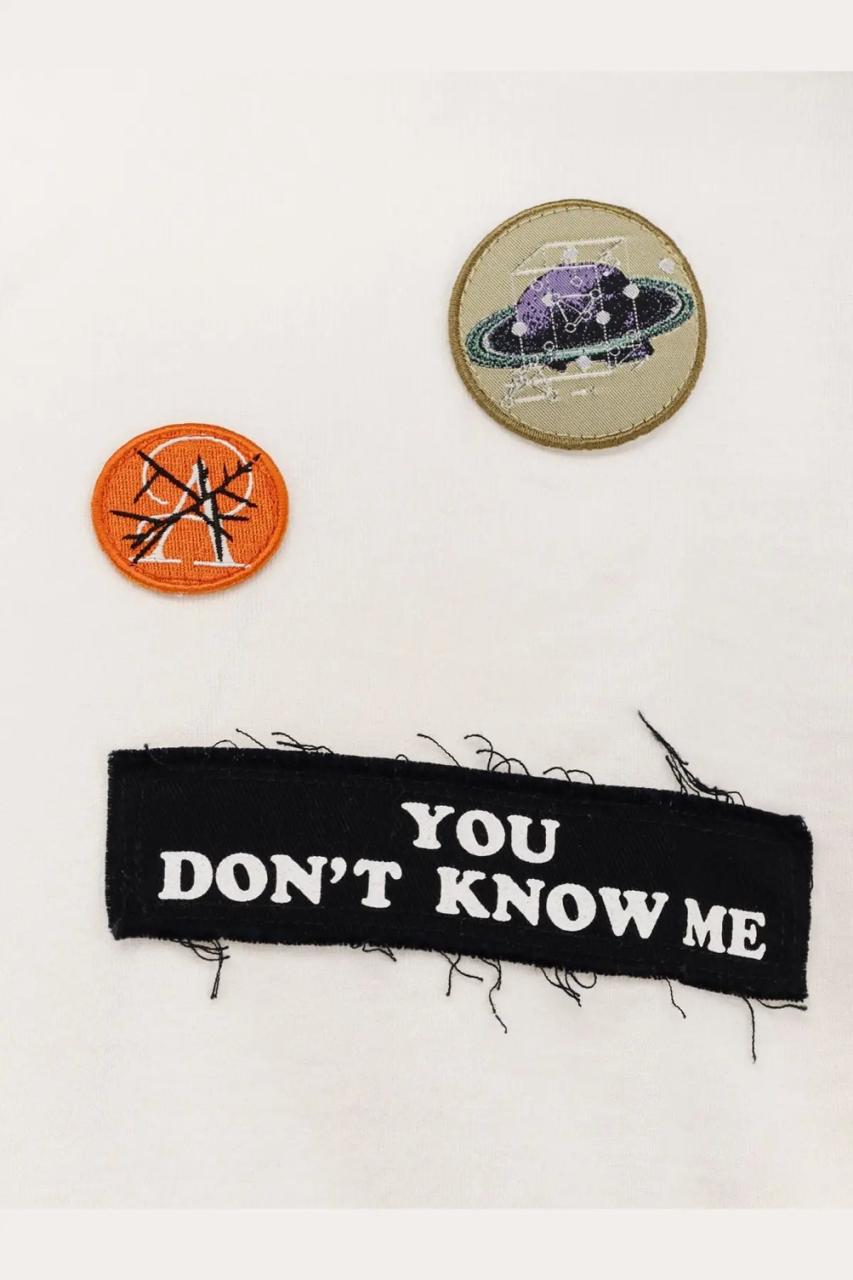 Black fabric patch with frayed edges and white embroidered text on the back of undercover men’s cotton white shirt