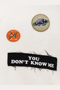 Black fabric patch with frayed edges and white embroidered text on the back of undercover men’s cotton white shirt