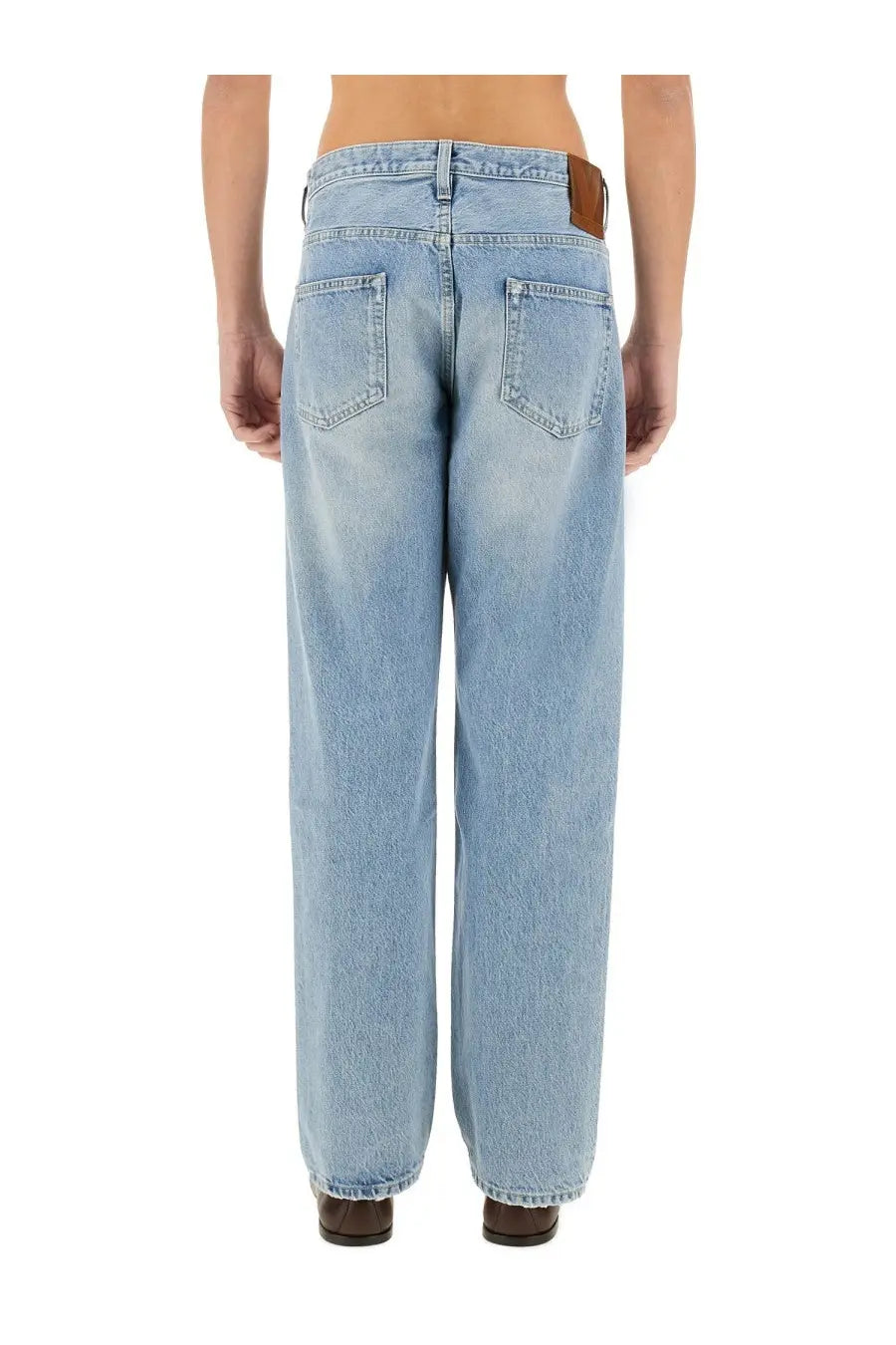 Light-wash denim jeans with wide-leg cut and brown leather brand patch at waistband shown from back side